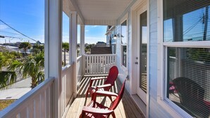 A covered porch with a white railing, red chairs, and a view of the neighborhood. - Home with rooftop beach views, winter open, snowbirds welcome! (Panama City Beach)