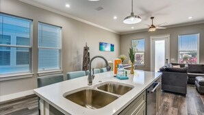 A modern kitchen with a central island, stainless steel sink, and overhead lighting. - Home with rooftop beach views, winter open, snowbirds welcome! (Panama City Beach)