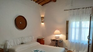 Une chambre à coucher avec un lit, une table de chevet, une lampe, une horloge murale et une fenêtre avec des rideaux.