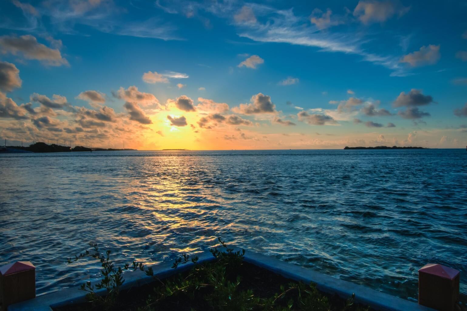 Un coucher de soleil sur une mer calme, avec une terre lointaine à l'horizon.