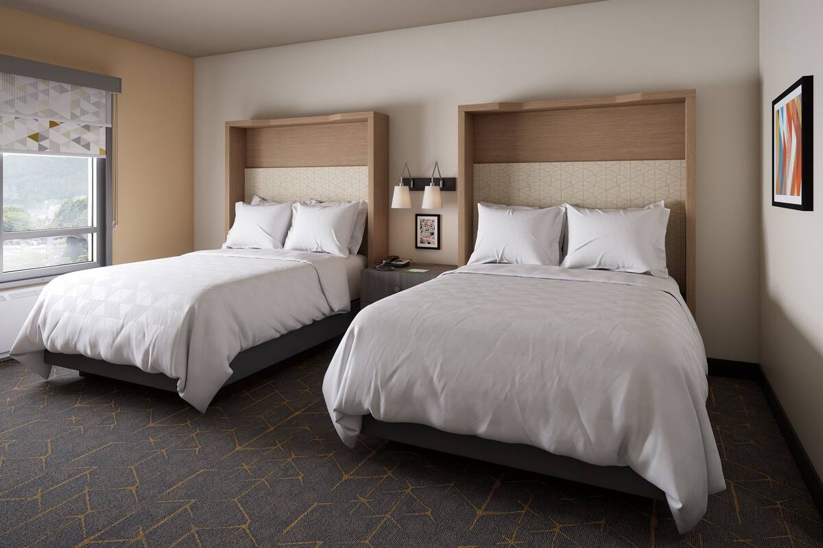 A hotel room with two beds, a window with a view, a nightstand, and a wall-mounted lamp.