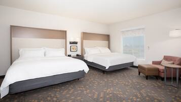 A hotel room with two beds, a small table, a chair, and a window.
