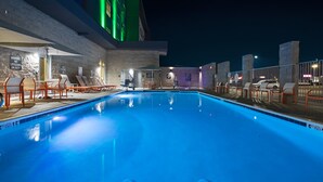 Una piscina nocturna con sillones de descanso y una estación de socorristas.