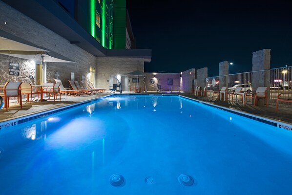 A nighttime swimming pool with lounge chairs and a lifeguard station.