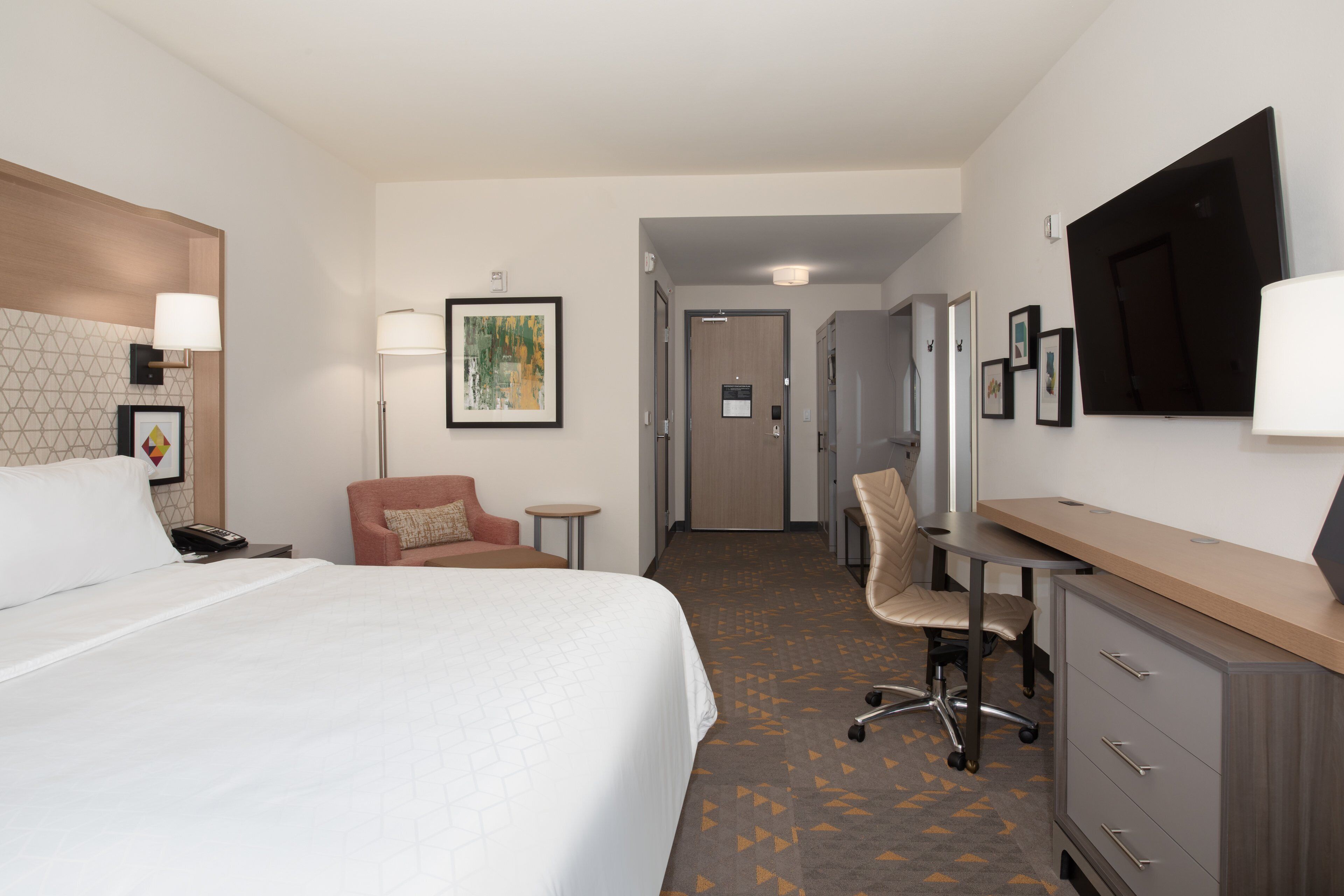 A hotel room with a large bed, a desk, a chair, and a TV.
