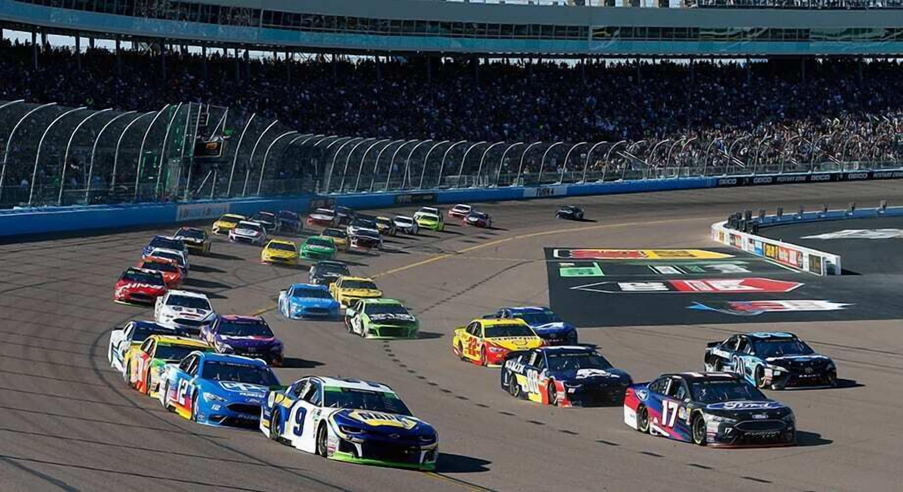 A racing event with multiple cars on a track, surrounded by a large audience in a stadium.
