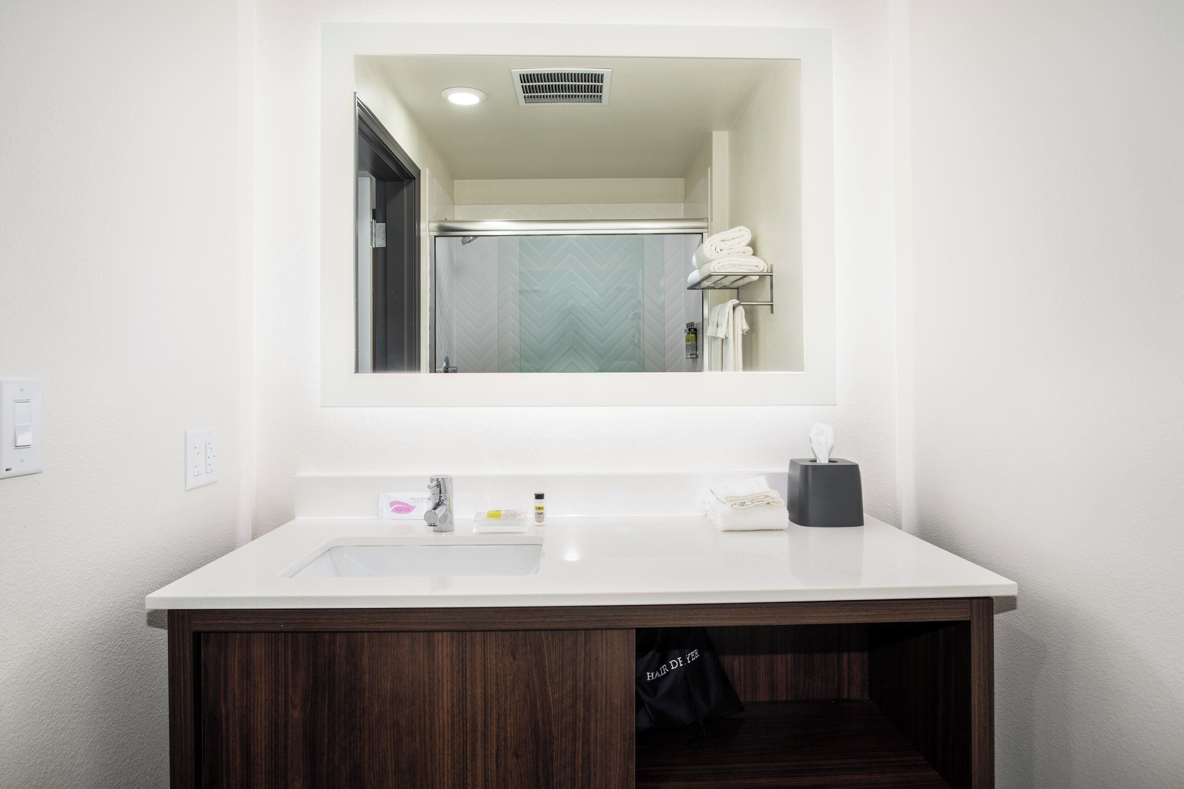 Un bagno moderno con un lavandino bianco, un mobile contenitore in legno scuro e uno specchio sopra il lavandino.