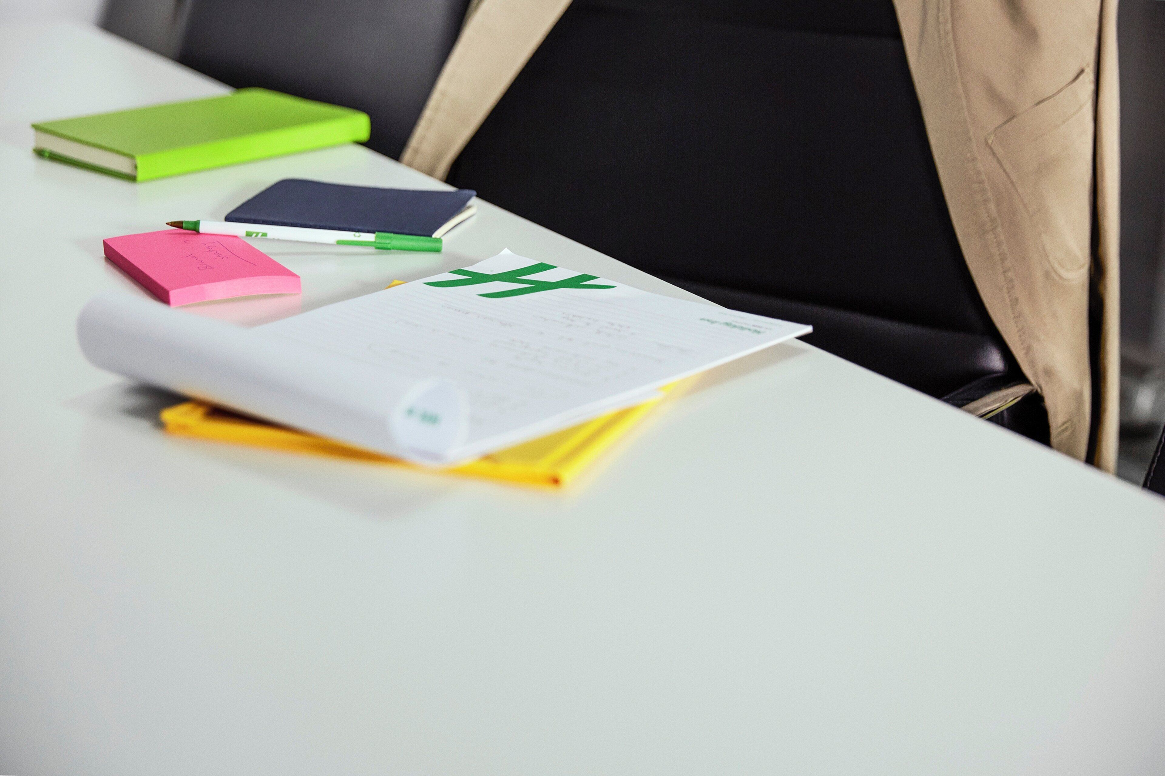 A white table with various office supplies like a green notebook, a pink sticky note, and a yellow notepad.