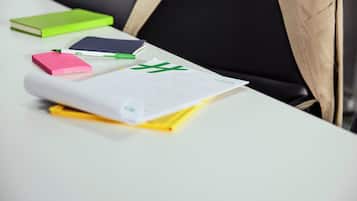 A white table with various office supplies like a green notebook, a pink sticky note, and a yellow notepad.