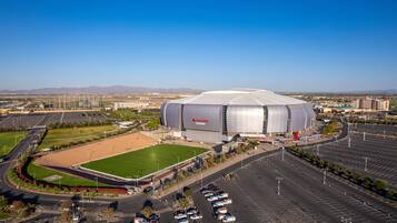 A large stadium with a covered seating area, a parking lot, and a baseball field.