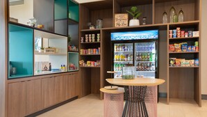 Una cafetería con mostrador de madera, exhibición de café y un refrigerador lleno de bebidas.