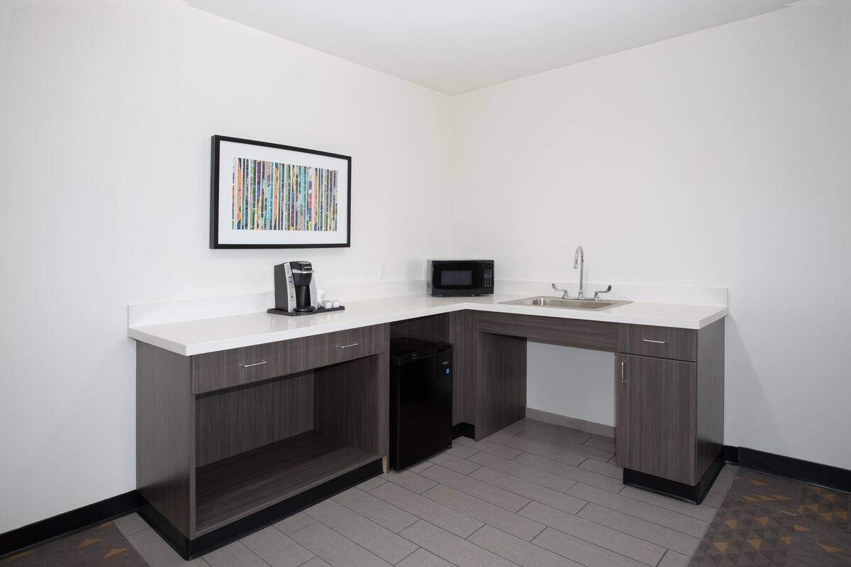 A compact kitchen with a white countertop, dark wood cabinets, a black dishwasher, a microwave, and a sink.