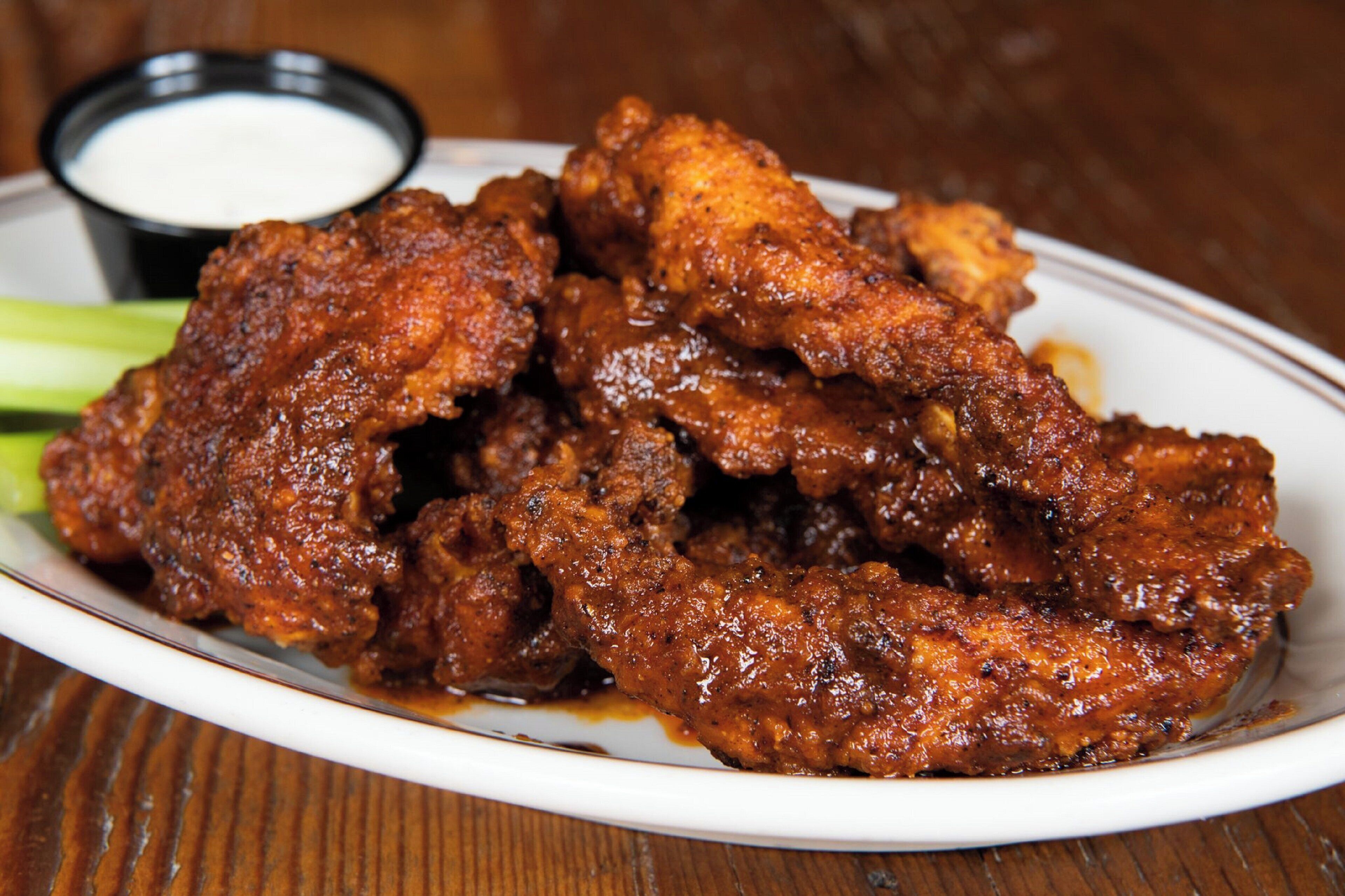 A plate of chicken wings with a dark sauce, accompanied by a small bowl of dipping sauce and celery sticks.