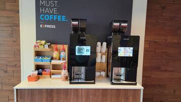 A coffee station with two espresso machines, a shelf with coffee products, and a sign that reads 'MUST. HAVE. COFFEE.'