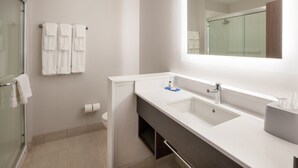 Un baño moderno con cabina de ducha de vidrio, un lavabo blanco con espejo y dos toallas blancas colgadas en la pared.