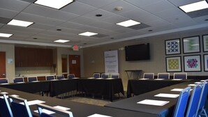 A conference room with tables, chairs, a flat-screen TV, and a sign indicating amenities. - Holiday Inn Express & Suites Murphysboro - Carbondale by IHG (Murphysboro)