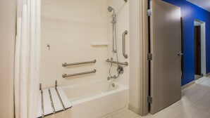 Un baño moderno con bañera a nivel del suelo, barras de apoyo y cabezal de ducha.