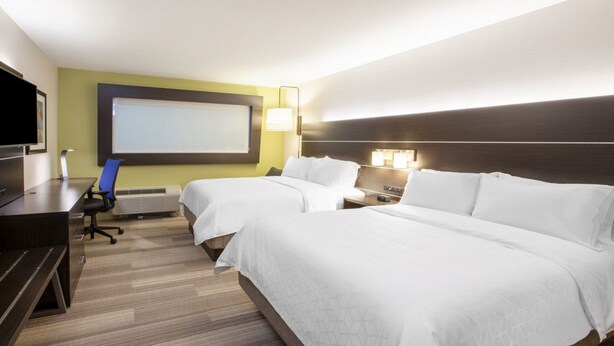 Habitación de hotel con dos camas, un escritorio, una silla, un televisor y una pantalla para proyector.