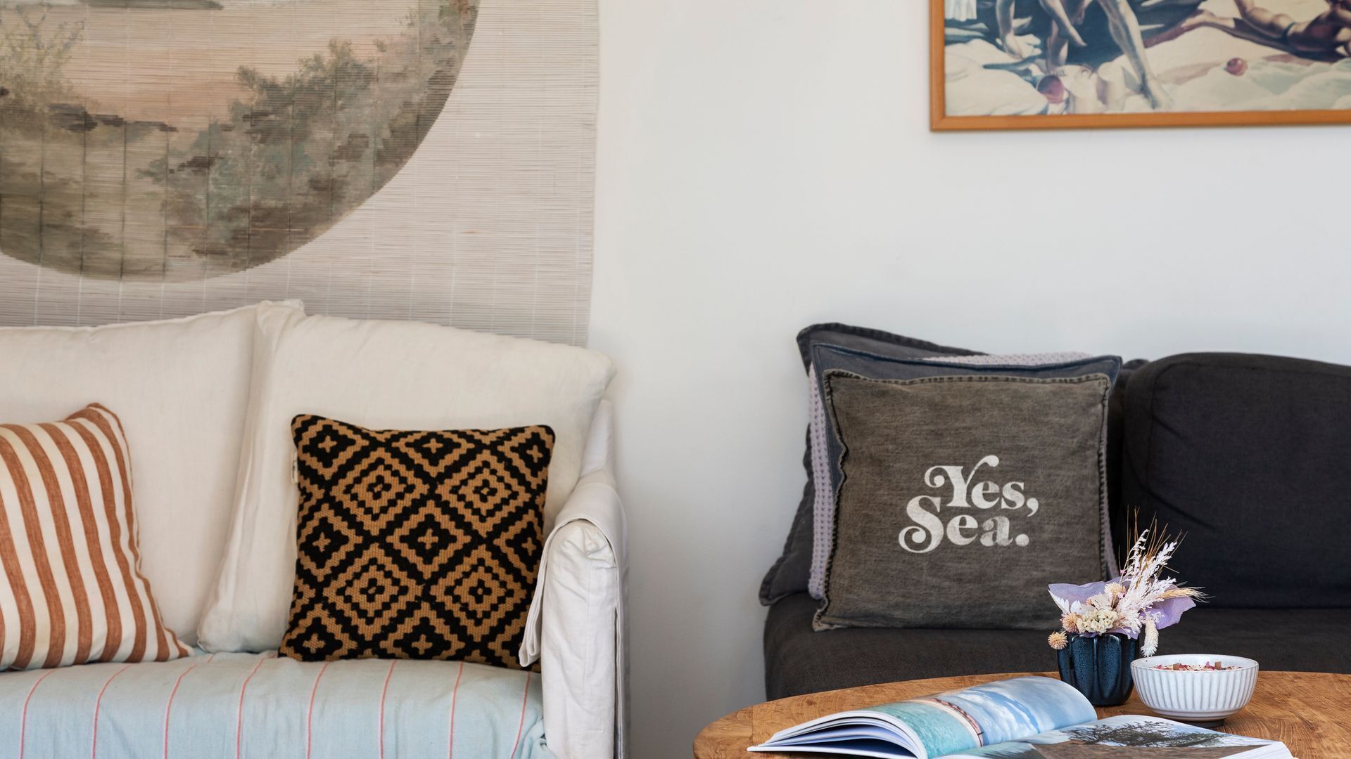 A living room with a sofa, two cushions, a coffee table with a book and a vase of flowers.