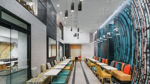 En modern restaurang med långa, gemensamma bord, avskilda sittplatser och en färgstark väggmålning på den högra väggen.