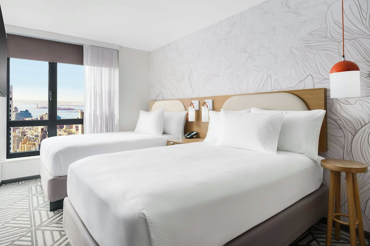 Habitación de hotel con dos camas, vistas a la ciudad, un revestimiento de pared con diseño de mármol y una mesita de noche de madera.