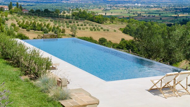 A rectangular swimming pool with a view of a rural landscape and mountains in the background.