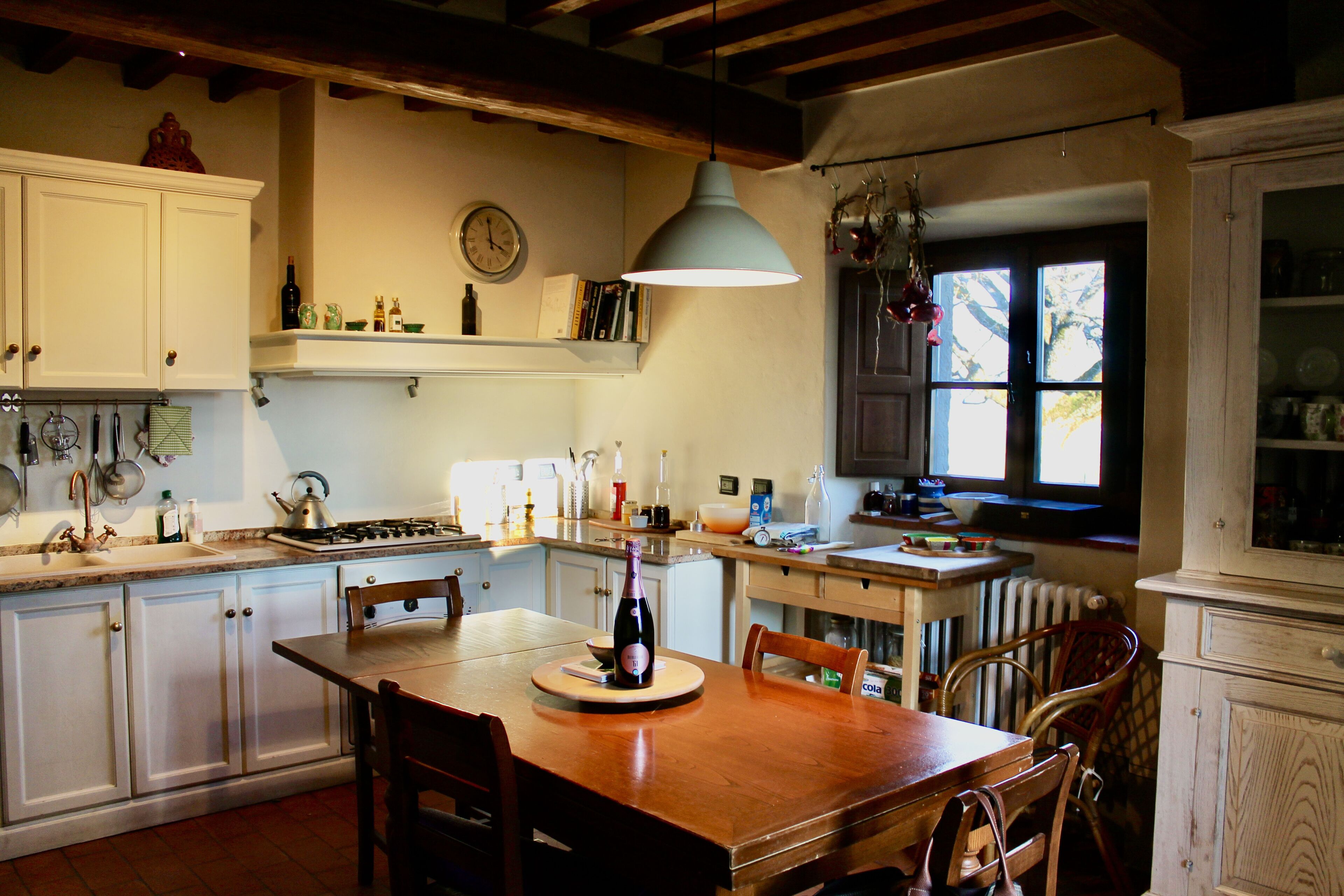 Una cocina con armarios blancos, una mesa de comedor de madera y una lámpara colgante.