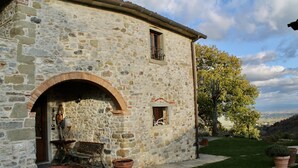 A stone building with an arched entrance, a small window with a balcony, and a bench outside.