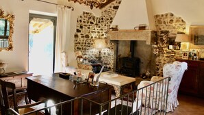 A rustic room with a stone wall, a fireplace, a wooden table, and a chandelier.