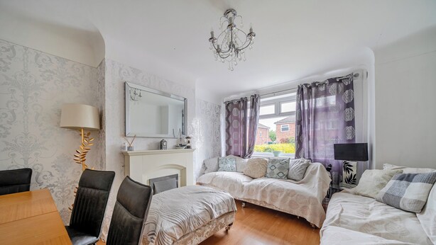 Ein Zimmer mit zwei Betten, einem Esstisch, Stühlen, einer Chandelier und einem Fenster mit Vorhängen.