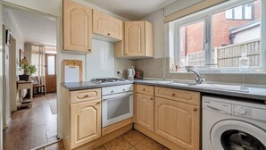 Eine Küche mit Holzausstattung, einem Gasherd, einem Backofen, einer Waschmaschine und einem Fenster mit Blick auf ein Backsteingebäude.
