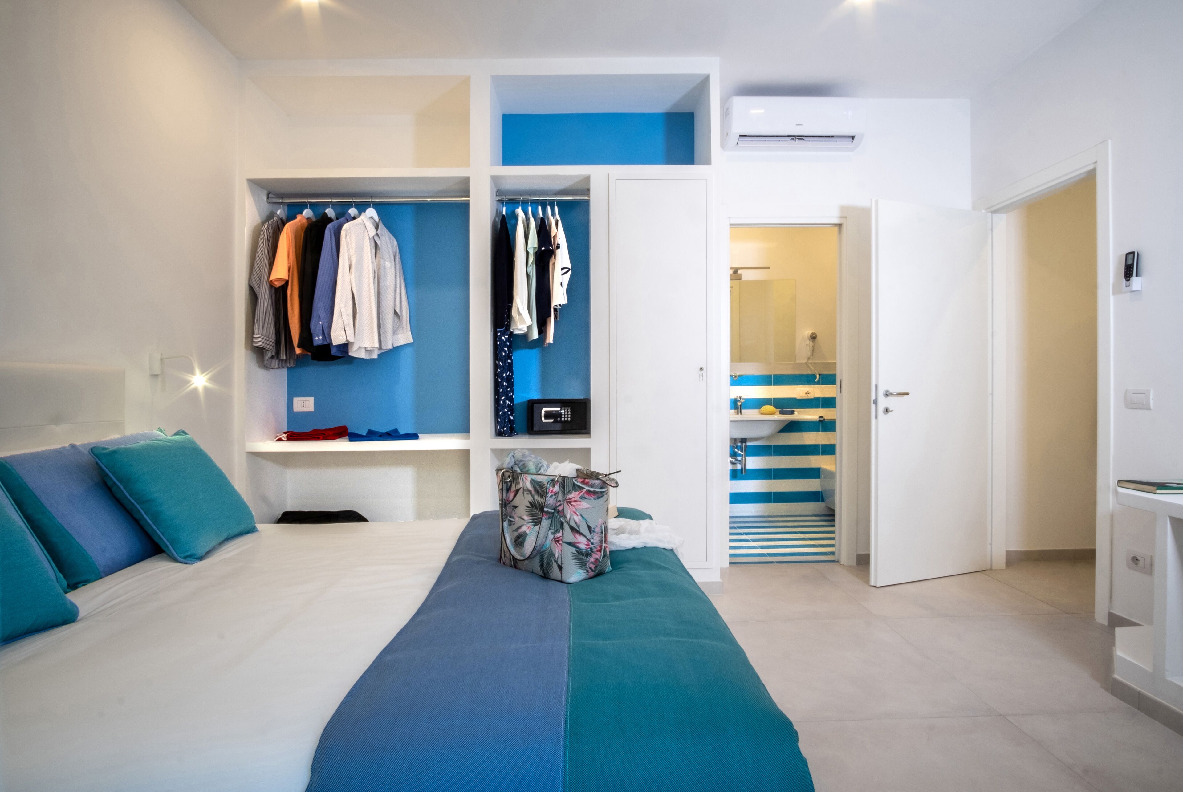 A modern bedroom with a bed, a wardrobe, and a bathroom visible through an open door.