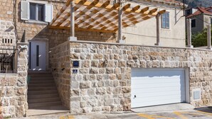 A stone building with a white garage door, a wooden pergola, and a staircase leading to the entrance. - Apartment Toma (Dubrovnik)