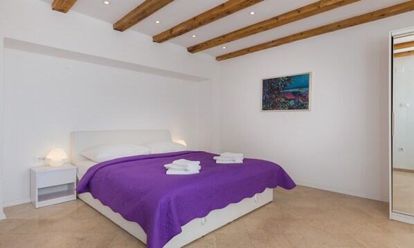 A bedroom with a bed, white nightstands, a purple bedspread, and a painting on the wall.