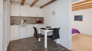 A compact kitchen with white cabinets, a microwave, and a sink. There is a small table with two chairs and a clock on the wall. - Apartment Toma (Dubrovnik)