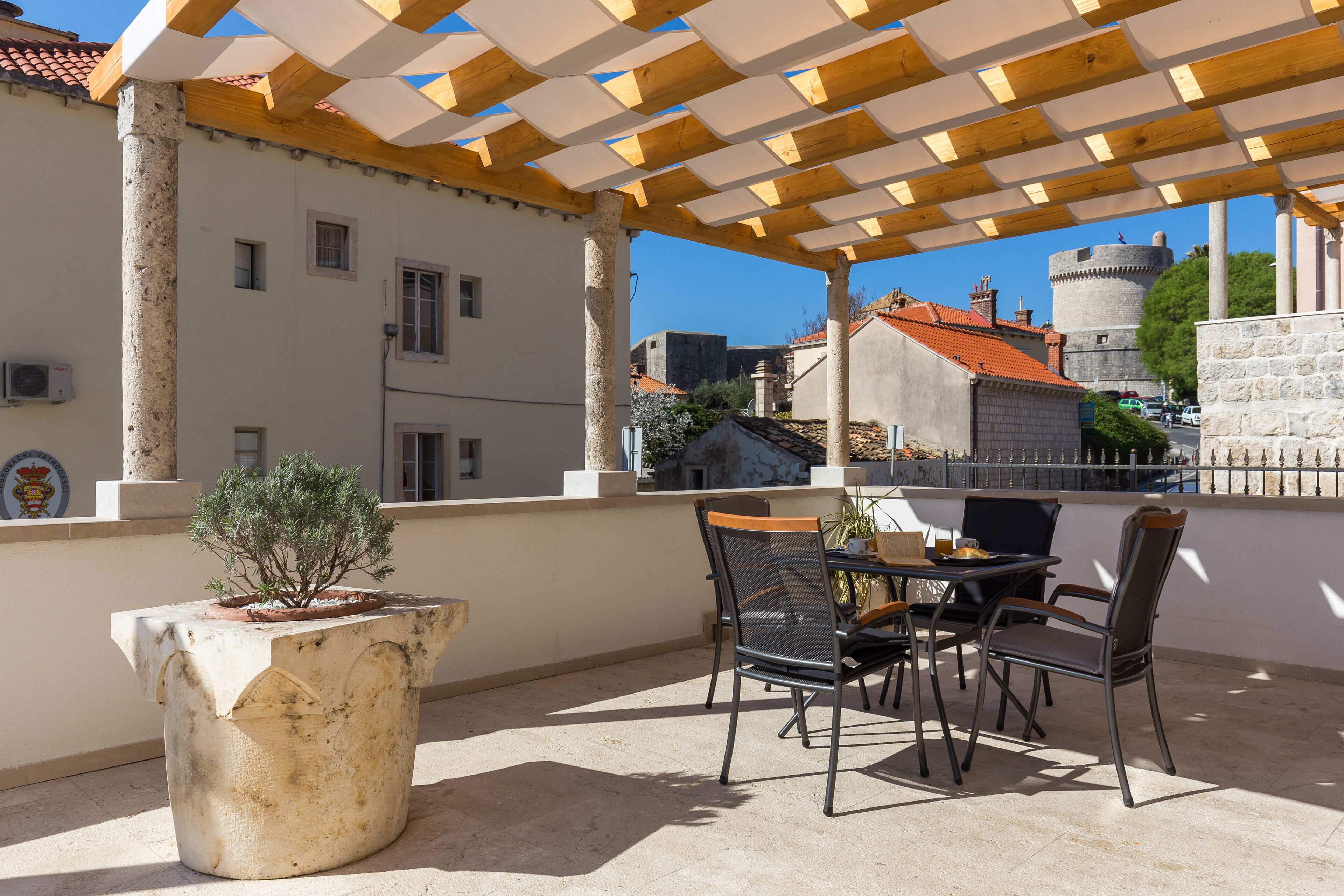 A terrace with a table and chairs, a potted plant, and a view of a castle in the background.