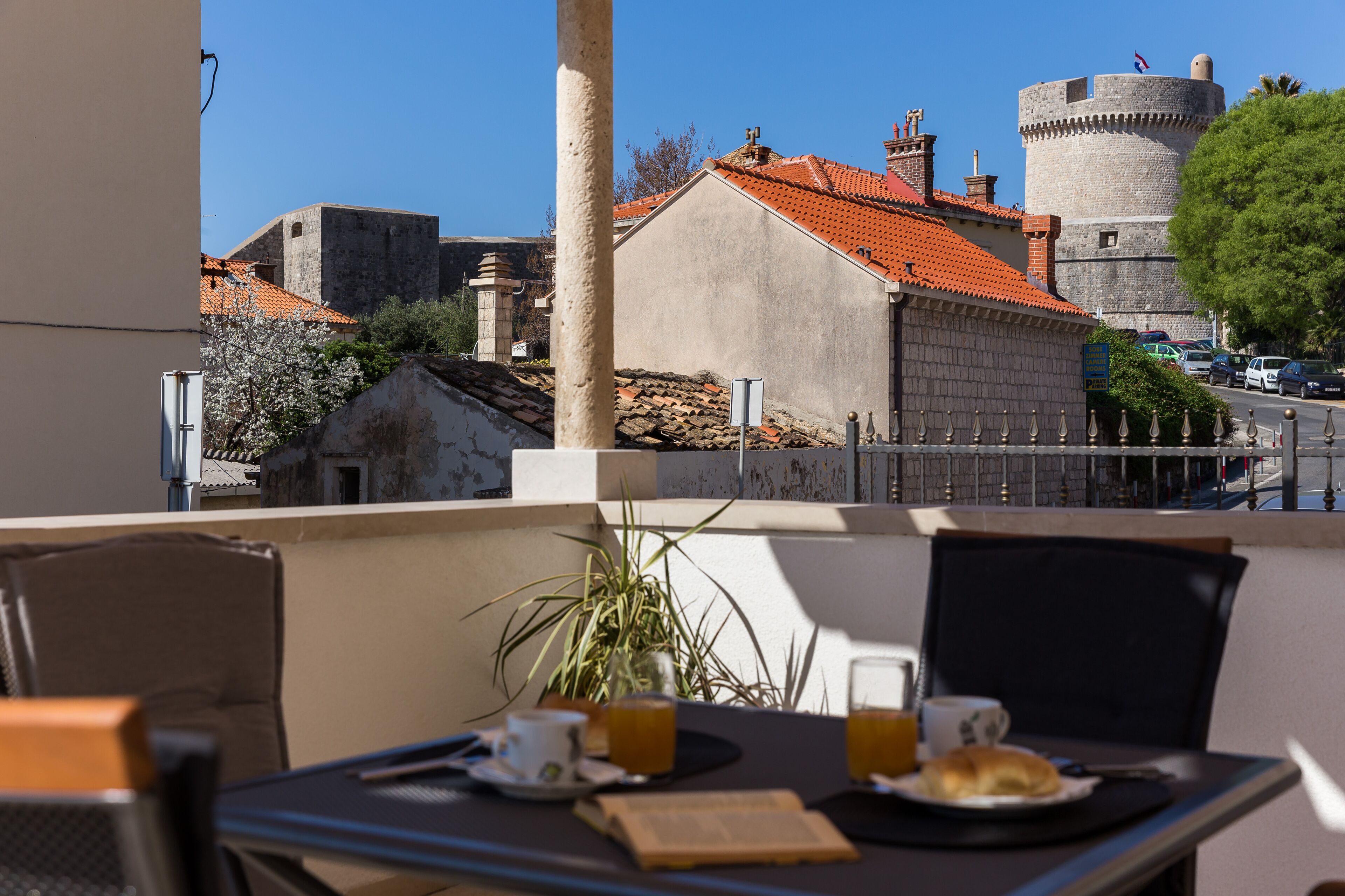 A balcony with a table set for breakfast, overlooking a historic town with stone buildings and a castle.