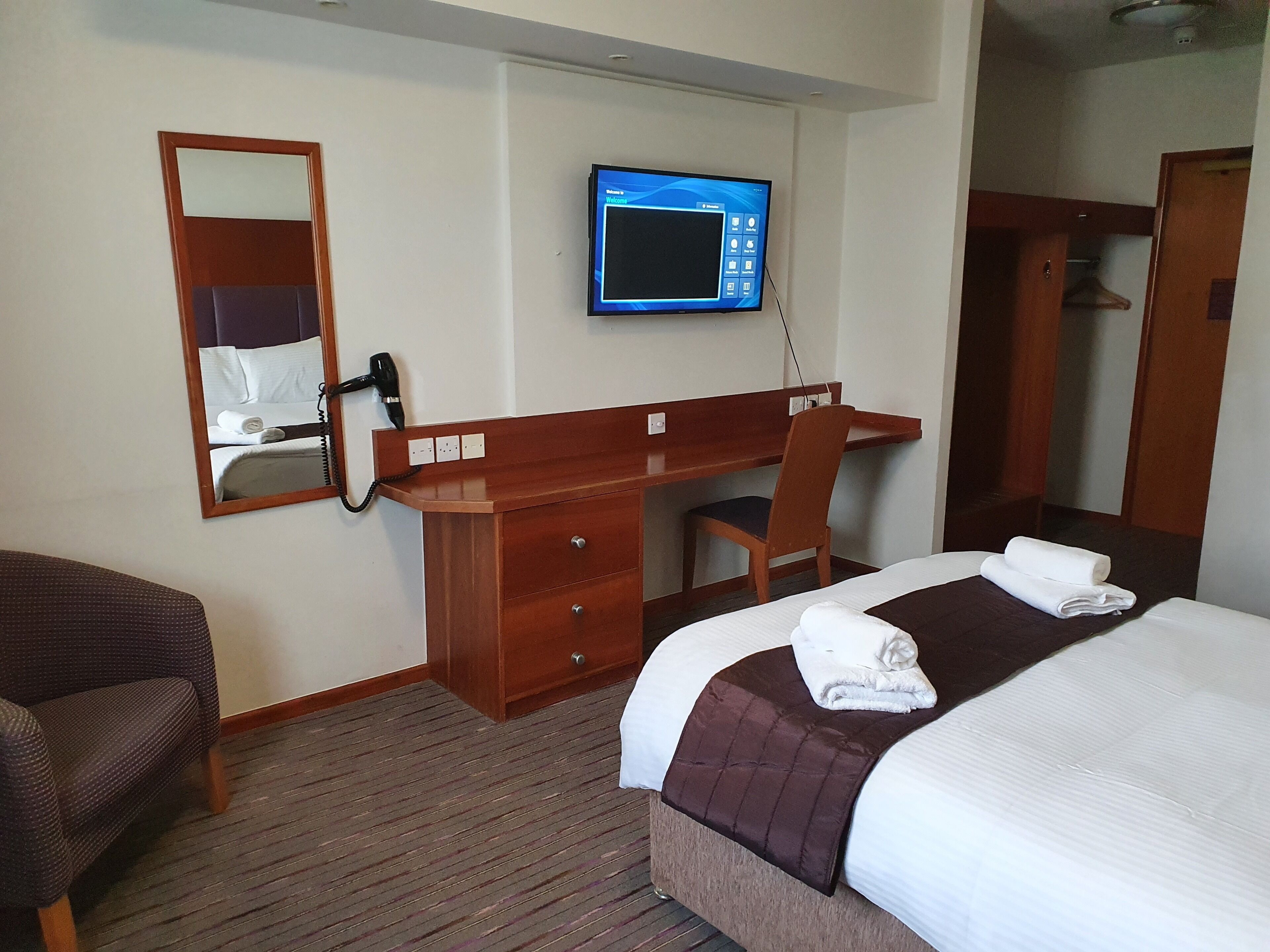 Une chambre d’hôtel avec un lit, un bureau, une chaise, une télévision et un miroir.