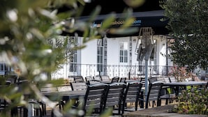 Outdoor seating with tables and chairs, a building with a sign, and a stone wall.