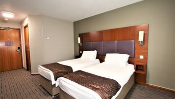 A hotel room with two beds, a wooden headboard, and a nightstand with a lamp.