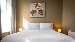 A large bed with white linens, a wall-mounted artwork of flowers, and two bedside lamps.