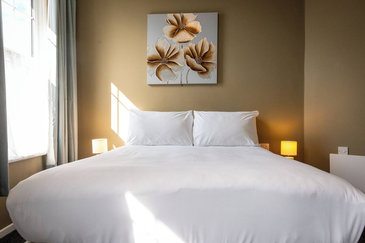 A large bed with white linens, a wall-mounted artwork of flowers, and two bedside lamps.