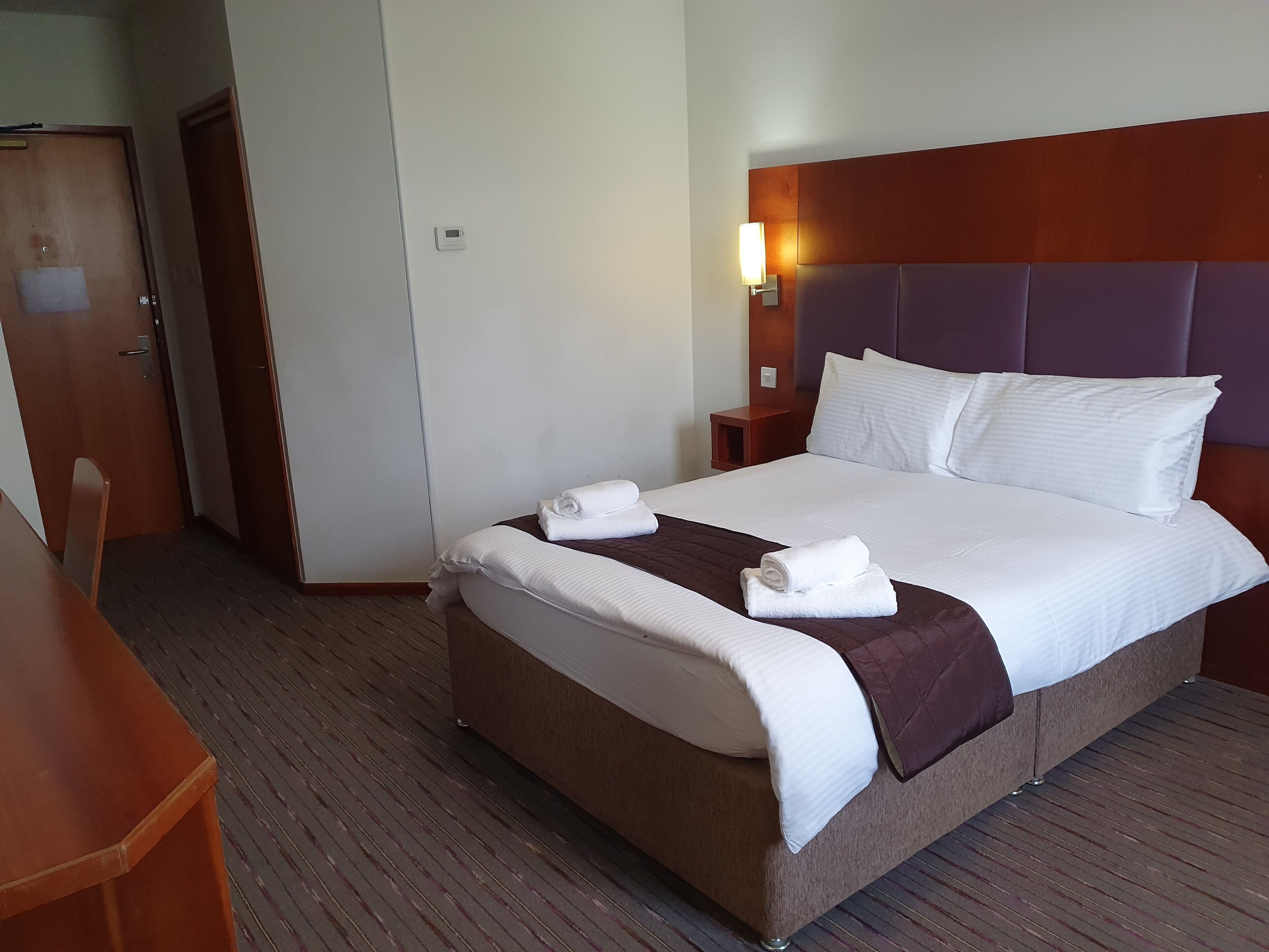 Una habitación de hotel con cama, mesita de noche y un escritorio de madera.