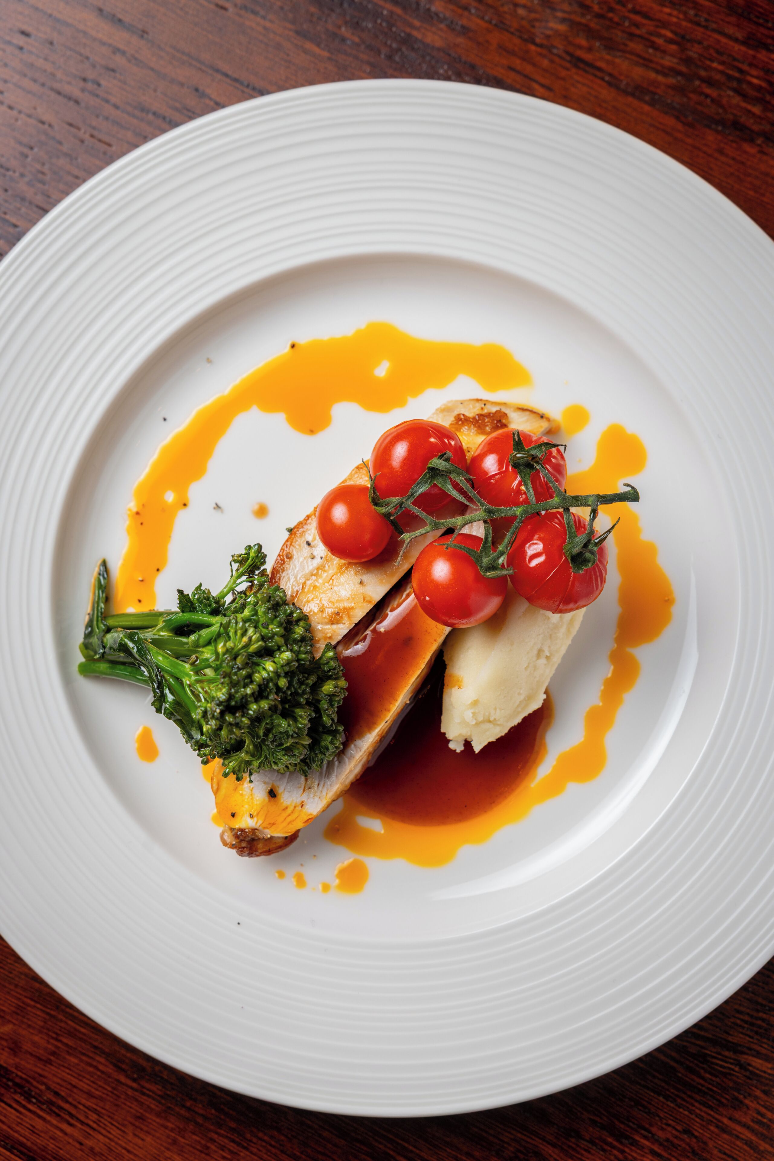 Un plato blanco con un trozo de pescado, tomates cherry y brócoli.