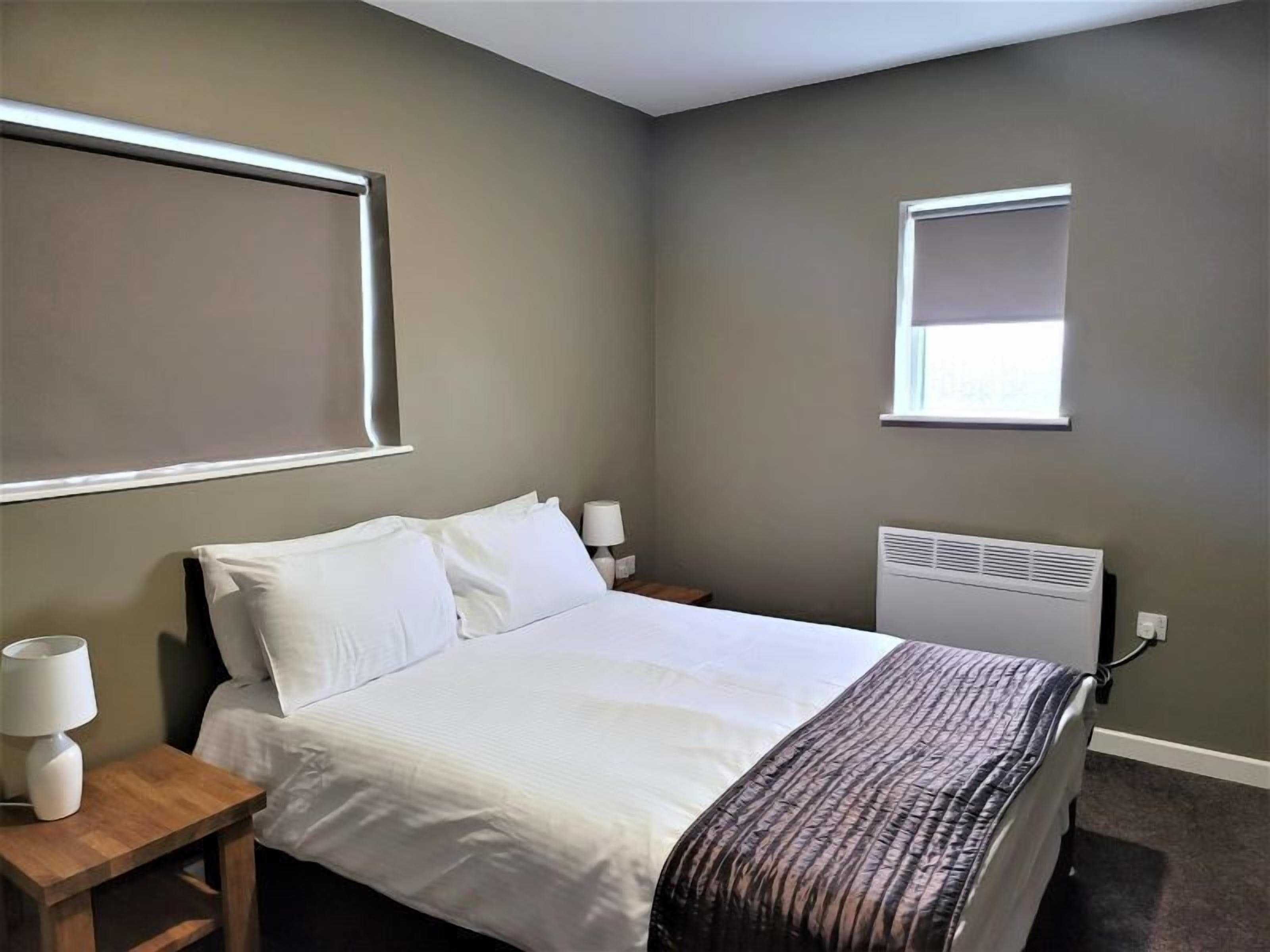 Un dormitorio con cama, mesitas de noche, ventana y un calentador de pared.