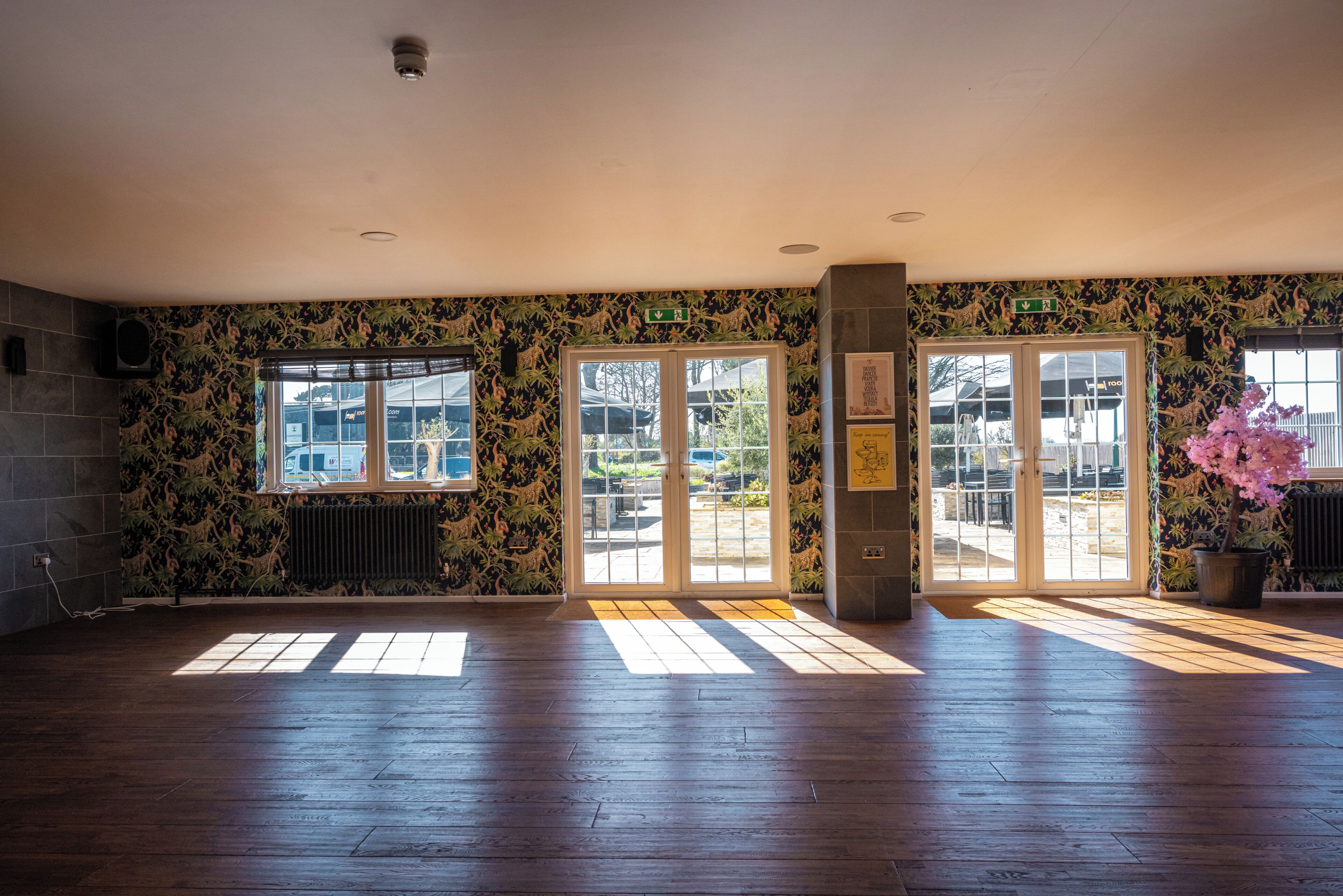 A spacious room with a wooden floor, large windows, and a door leading outside.