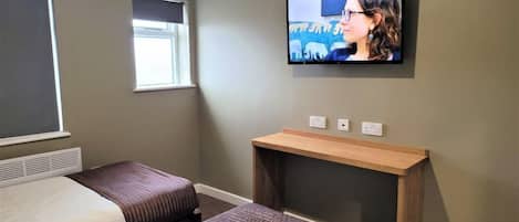 A hotel room with two beds, a TV mounted on the wall, a window, and a small wooden table.