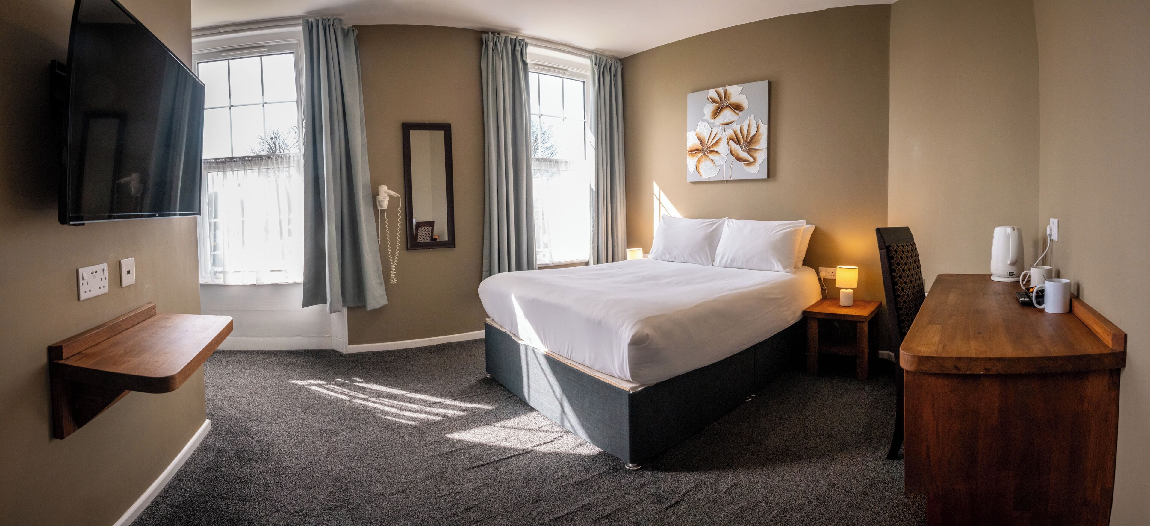 A hotel room with a bed, bedside table, lamp, and a flat-screen TV mounted on the wall.