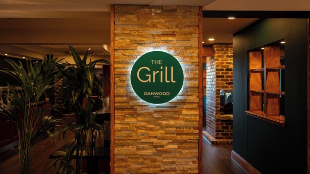 A hallway with a sign for 'The Grill Oakwood Hotel' on a stone wall.