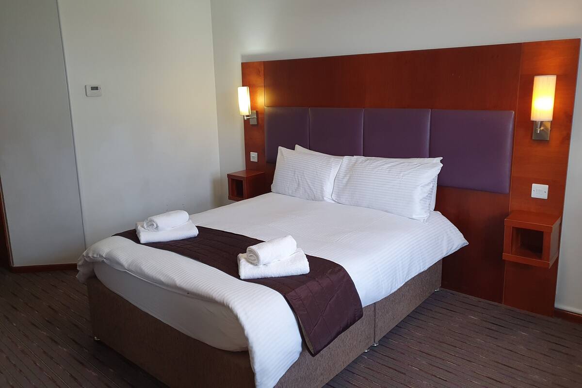 A neatly made bed with white linens and a brown blanket, two bedside tables with lamps, and a wooden headboard.